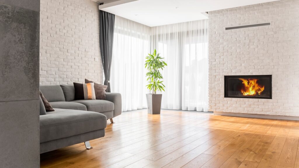 En stue med et rent, lysbrunt trægulv, en sofa og en pejs.