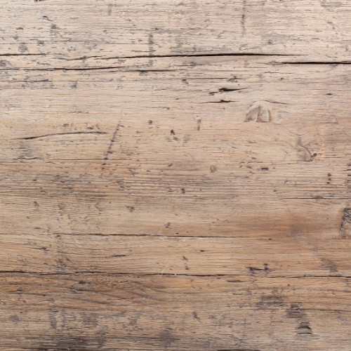 Close-up billede af en lys træbordplade med revner og ridser, der kan repareres med slibning.