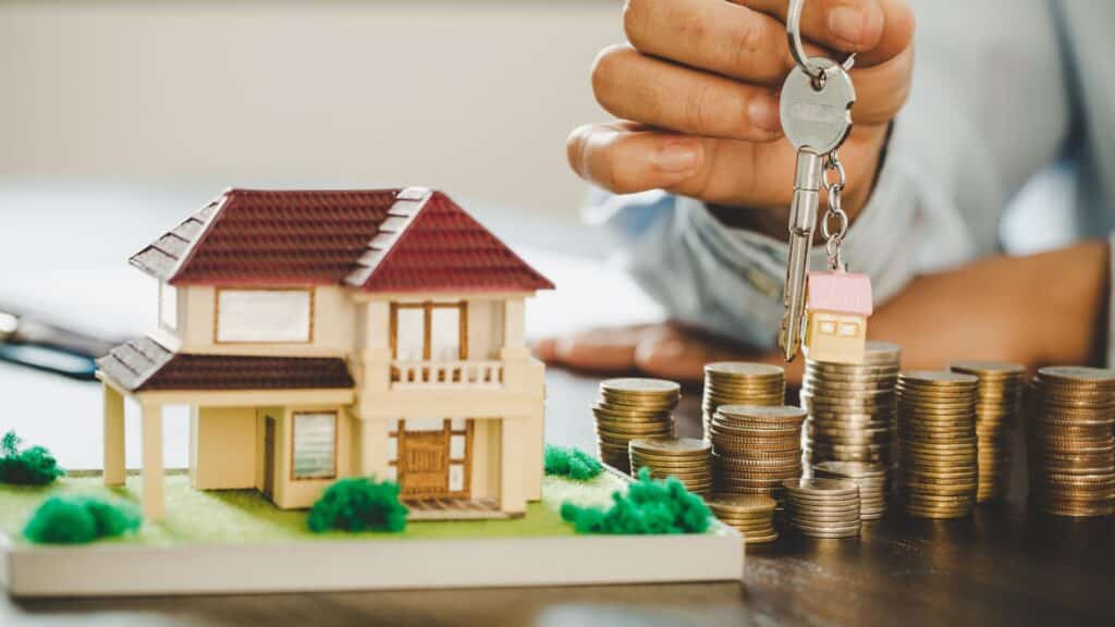 En detaljeret model af et hus legetøj omgivet af mønter spredt på en træbordsoverflade, der symboliserer et boligdepositum eller investering i ejendom.