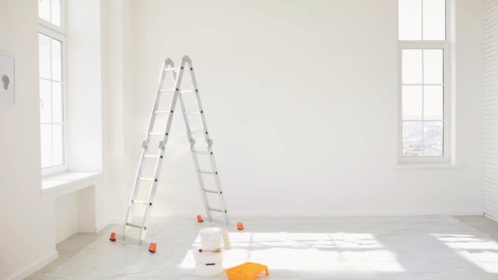 Et tomt værelse under istandsættelse ved fraflytning med en stige og en spand hvid maling placeret på gulvet.