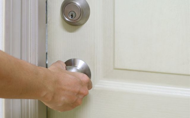 En persons hånd lukker døren til et rum, der ikke skal slibes, for at forhindre støv i at trænge ind - en smart måde at spare tid på rengøring efter gulvafslibning.