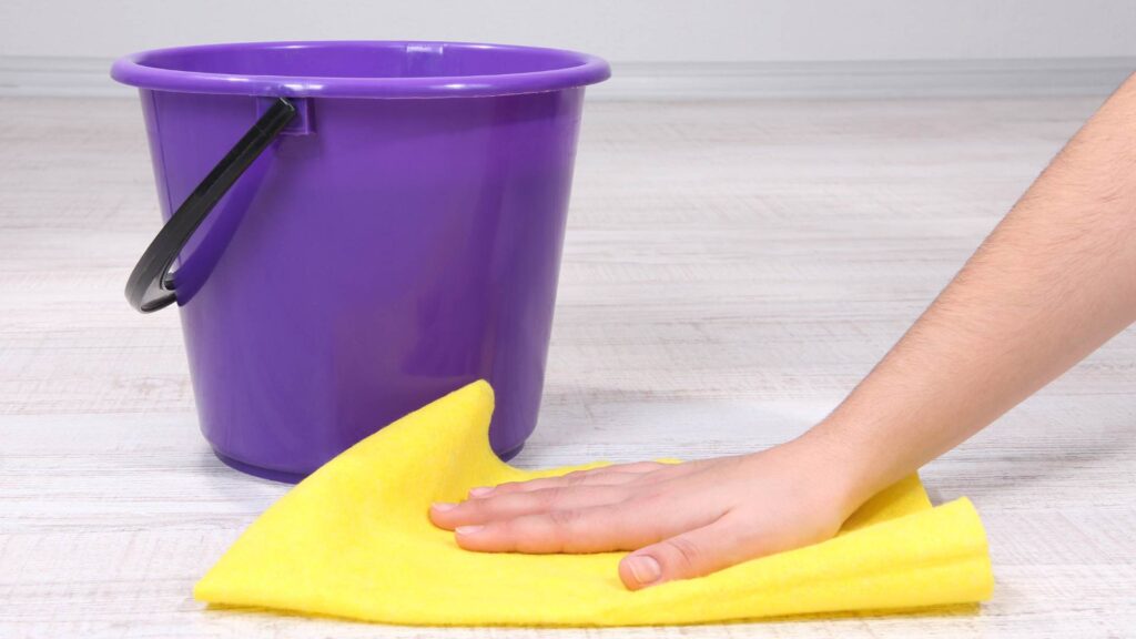 Vask trægulvet af en menneskelig hånd, der holder en gul klud