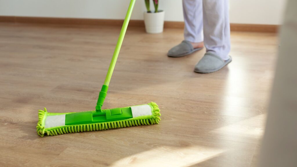 En person vasker et lyst gulv med en grøn moppe